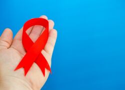 rote AIDS-Schleife auf Hand liegend vor blauem Hintergrund