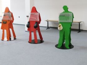 Ausschnitt der Ausstellung zeigt 5 lebensgroße Figuren in orange, rot, grün, gelb mit verschiedenen Utensilien