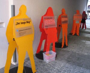 Fünf Figuren der Ausstellung "Der lange Weg" sind an einer Mauer zu sehen.