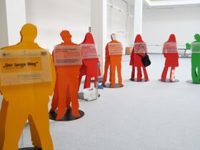 Ausschnitt der Ausstellung zeigt 7 lebensgroße Figuren in orange, rot, grün